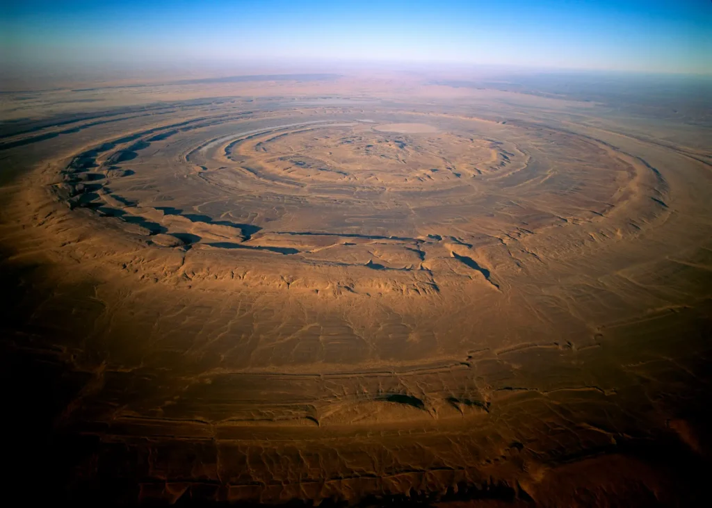 Aerial view of the Richat Structure, also known as the Eye of the Sahara, located in the Guelb region of Mauritania. The structure appears as concentric circular ridges, resembling a bullseye, with distinct layers of rock formations.