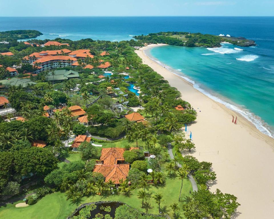 Aerial view of Grand Hyatt Bali beachfront resort in Nusa Dua with tropical gardens, white sand beach, turquoise ocean, and luxury villas along the coastline.