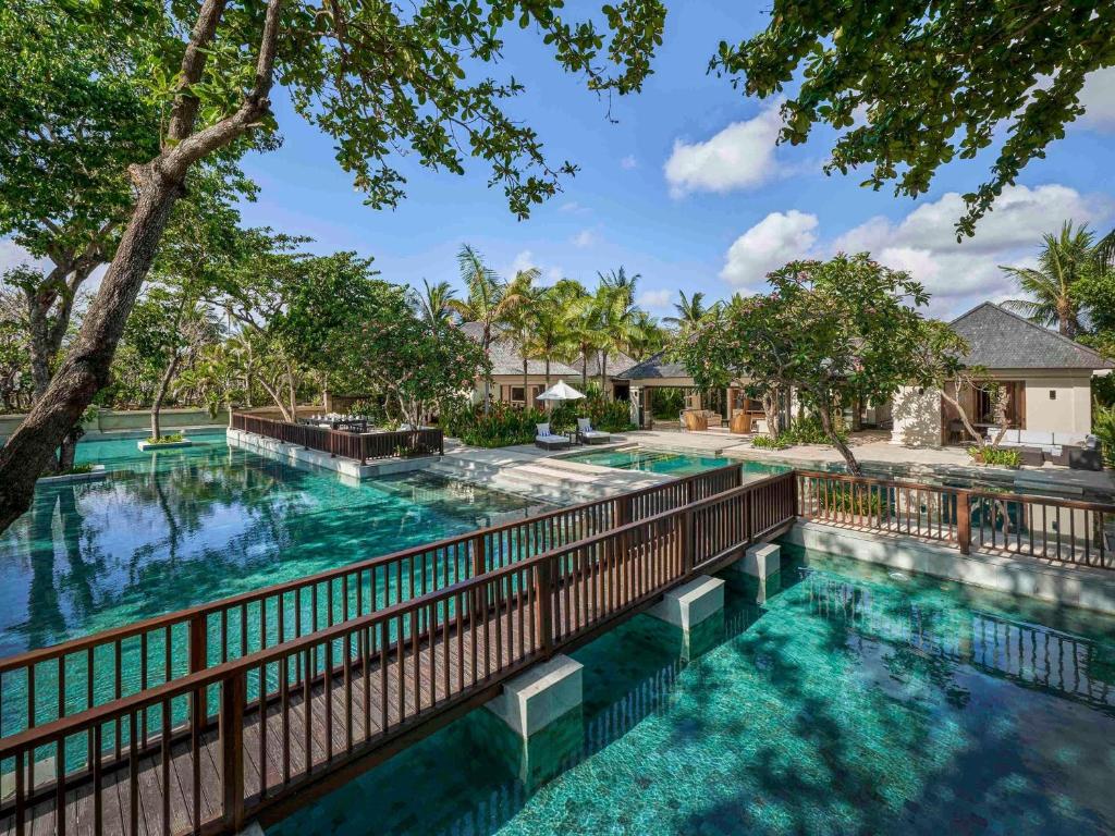 Large tropical lagoon-style swimming pools surrounded by palm trees and luxury villas at Sofitel Bali Nusa Dua Beach Resort in Bali, Indonesia.