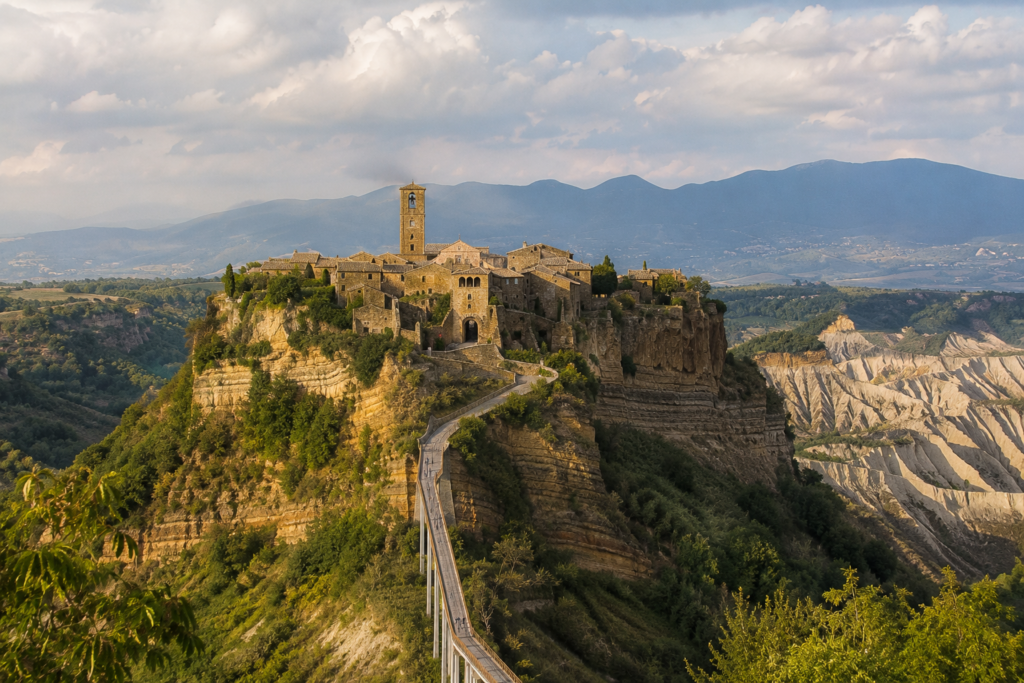 Hidden Gems in Europe - Civita di Bagnoregio, Italy ancient hilltop village perched on rocky cliffs with stone buildings, bell tower, narrow bridge, and sweeping countryside views.