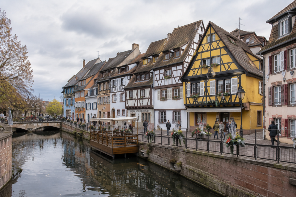 Hidden Gems in Europe - Colmar, France picturesque canal lined with colorful half-timbered houses, flower-filled balconies, cobblestone streets, and reflections in calm water.