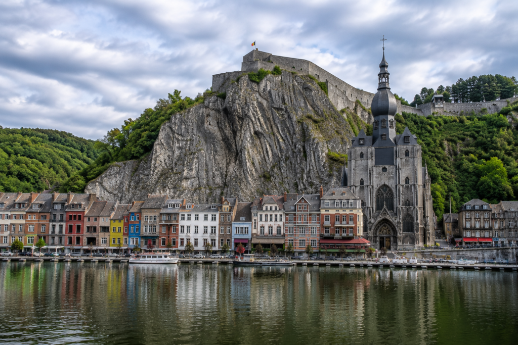Hidden Gems in Europe - Dinant, Belgium riverside town with colorful historic buildings, gothic cathedral, steep cliffs, and reflections on the Meuse River.