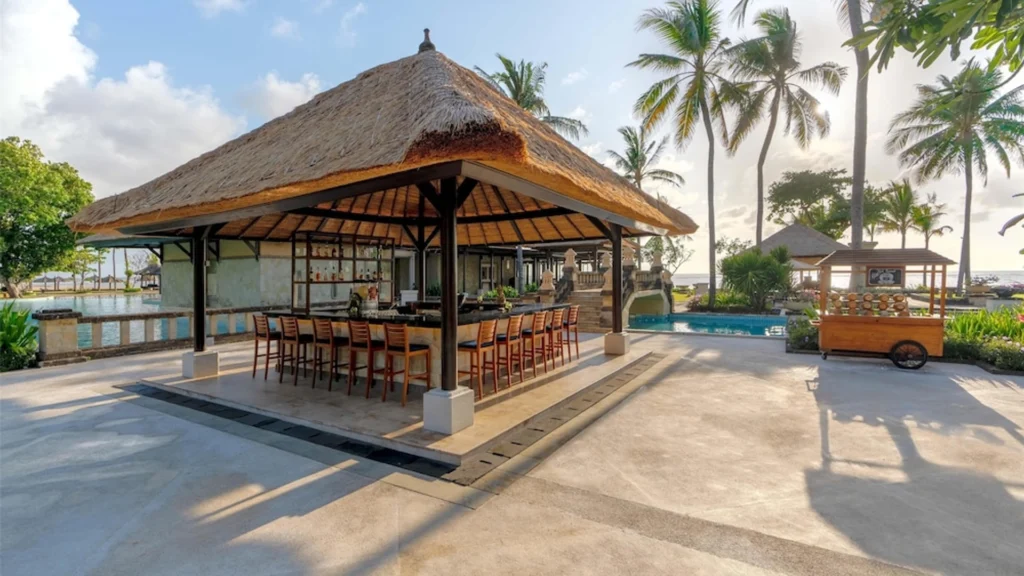 Open-air beachfront pavilion at Conrad Bali in Nusa Dua surrounded by palm trees, tropical gardens, and luxury resort facilities during golden hour.