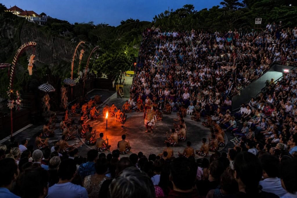 Kecak fire dance performance at Uluwatu, Bali, with performers gathered around a glowing fire and a large crowd seated in the open-air amphitheatre at dusk.