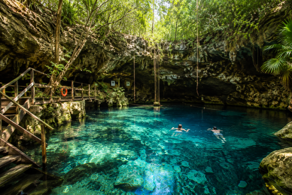 Guide to Tulum - Swimmers exploring a clear turquoise cenote surrounded by limestone caves and tropical jungle near Tulum, Mexico.