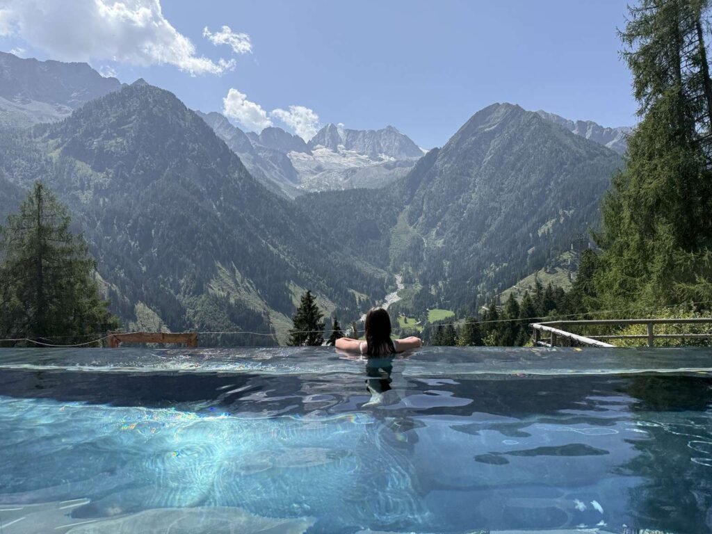 Chalet Al Foss pool view overlooking the presanella glacier and mountain alps with woman facing towards them