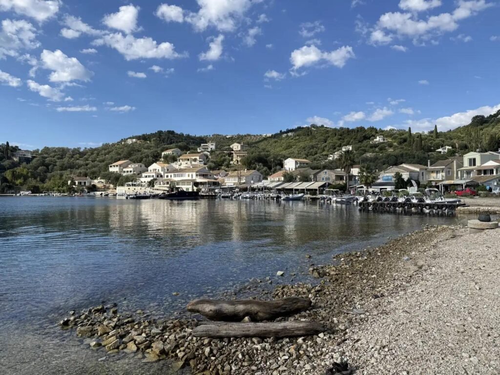 Peaceful harbour in Agios Stefanos Sinies, Corfu, with fishing boats, waterfront tavernas and green hills overlooking the bay.