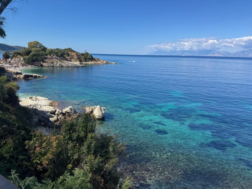Crystal-clear turquoise waters along the rocky coastline of Kassiopi, Corfu, with green headlands and views across the Ionian Sea.